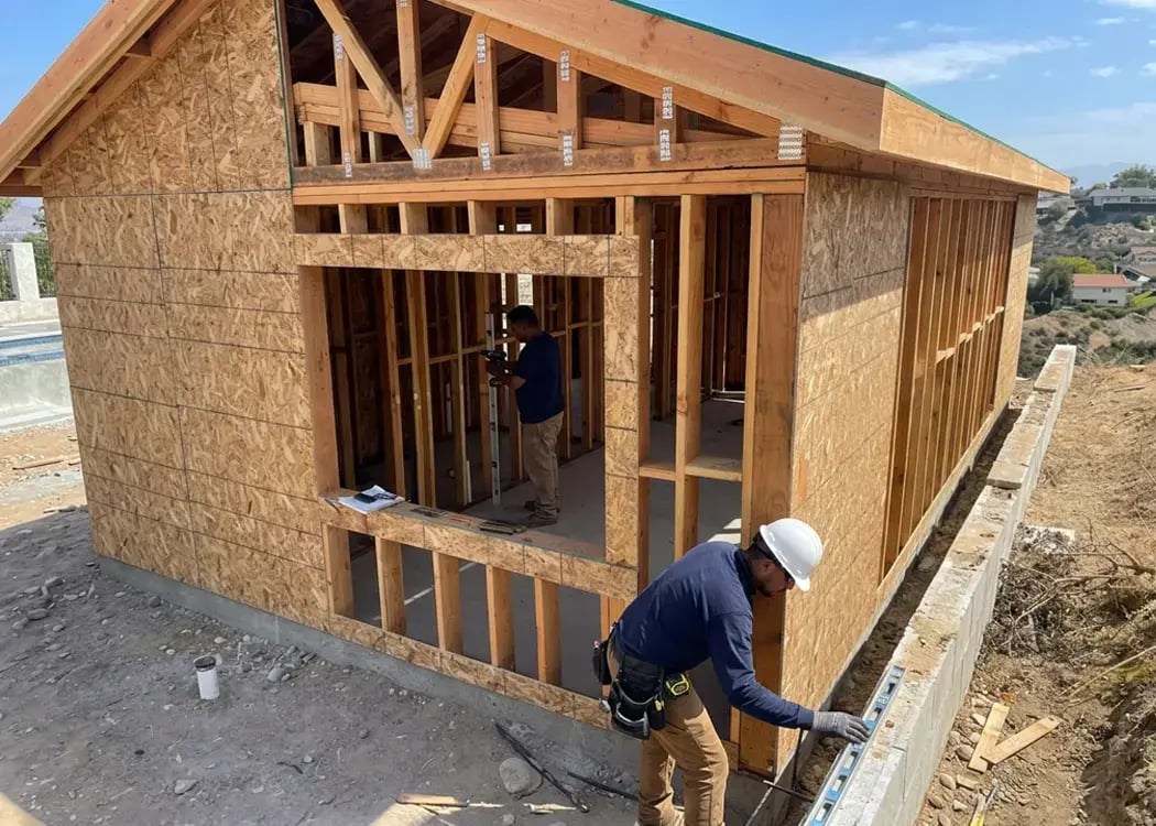 Detached ADU wall framing with OSB sheathing under construction as a worker squares up the foundation line