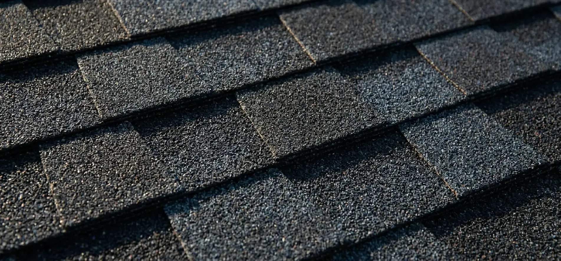Close-up of dimensional charcoal architectural asphalt shingles with layered tabs on a residential roof