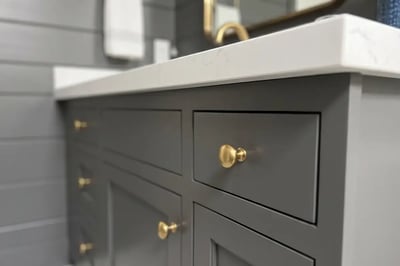 Charcoal shaker vanity fronts with brass knobs and a white quartz top after a full bathroom replacement