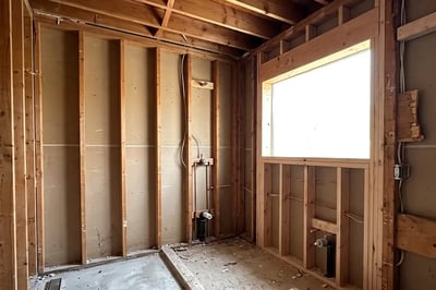 Bathroom stripped to studs and joists with drain stubs and framed window during full gut renovation
