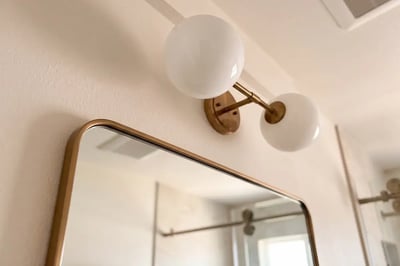Bronze framed mirror corner and opal glass globe sconce after a bathroom refresh — Hybrid Renovations