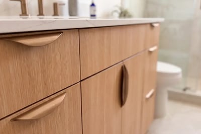 White oak vanity fronts with curved bronze pulls and a quartz countertop edge after a bathroom refresh