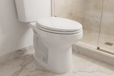 White two-piece toilet beside a marble-look tiled shower curb after a bathroom refresh