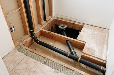 Black ABS drain lines and toilet flange rerouted for a bathroom remodel layout change — Hybrid Renovations
