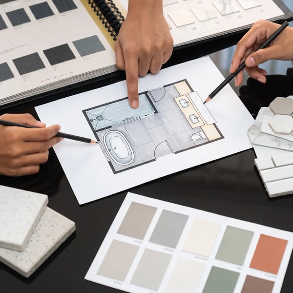 Hands over a bathroom floor plan with tile samples and paint chips at a remodel design consultation