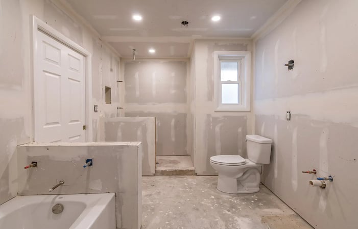 Taped drywall, a formed shower curb and plumbing stub-outs in a bathroom under construction — Hybrid Renovations