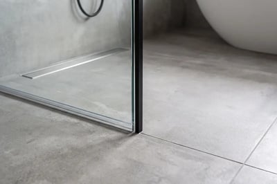 Frameless glass shower panel and linear drain after bathroom remodel with concrete-look tile