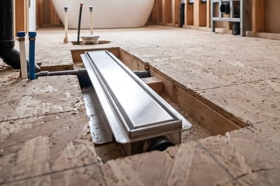 Stainless linear shower drain set into cut subfloor during bathroom gut renovation — Hybrid Renovations general contractor