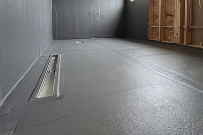 Gray waterproofing membrane and stainless linear drain installed ahead of tile in a bathroom remodel — Hybrid Renovations