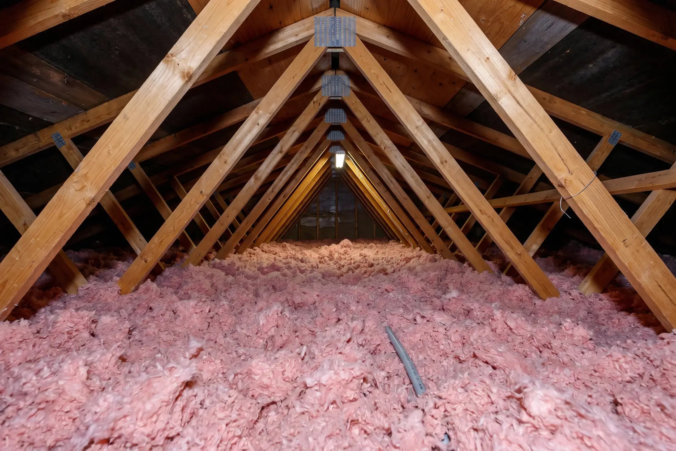 Blown-in fiberglass attic insulation installed between roof trusses for improved home energy efficiency.