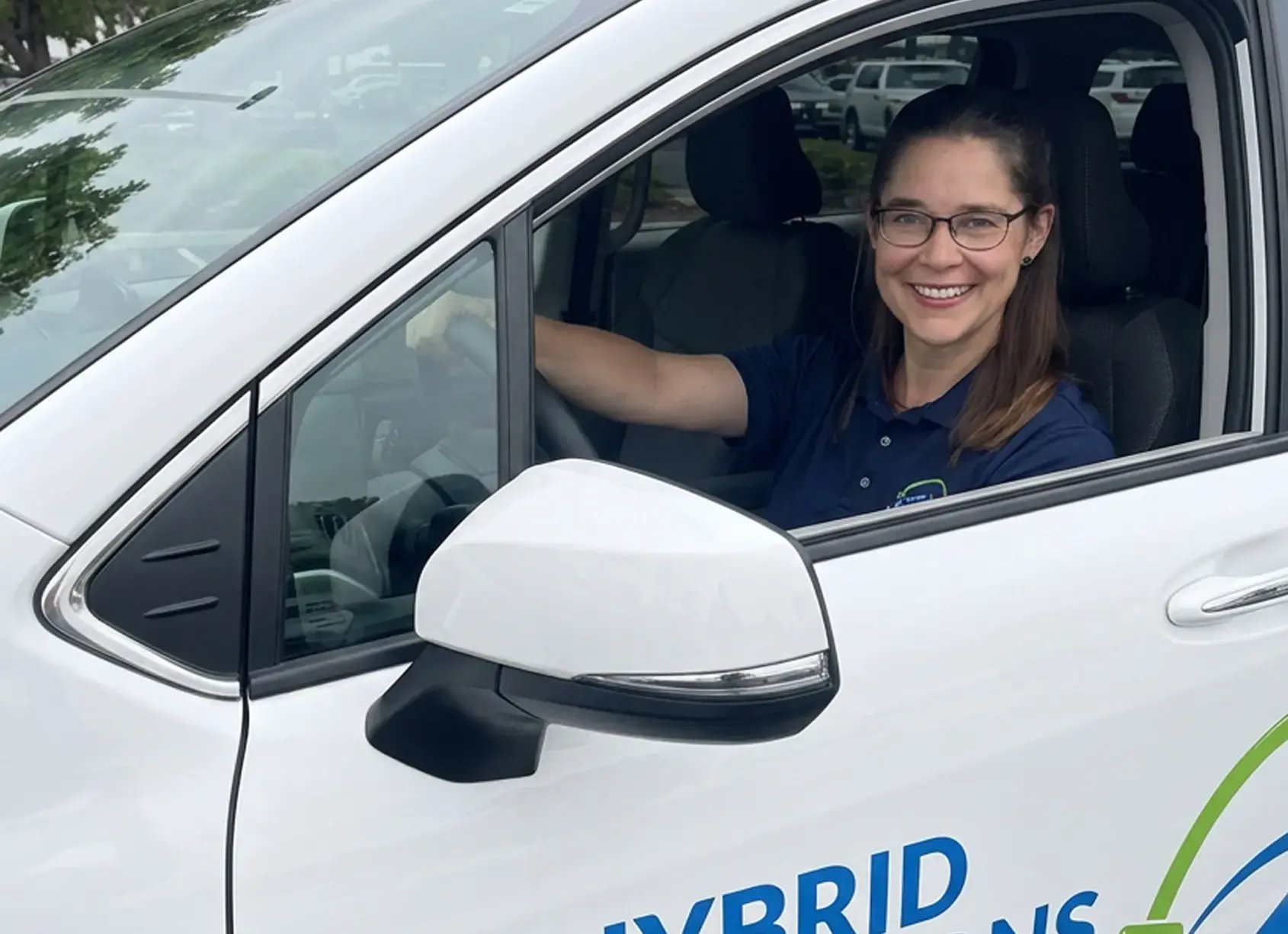Smiling Hybrid Renovations team member in a branded polo at the wheel of a company vehicle