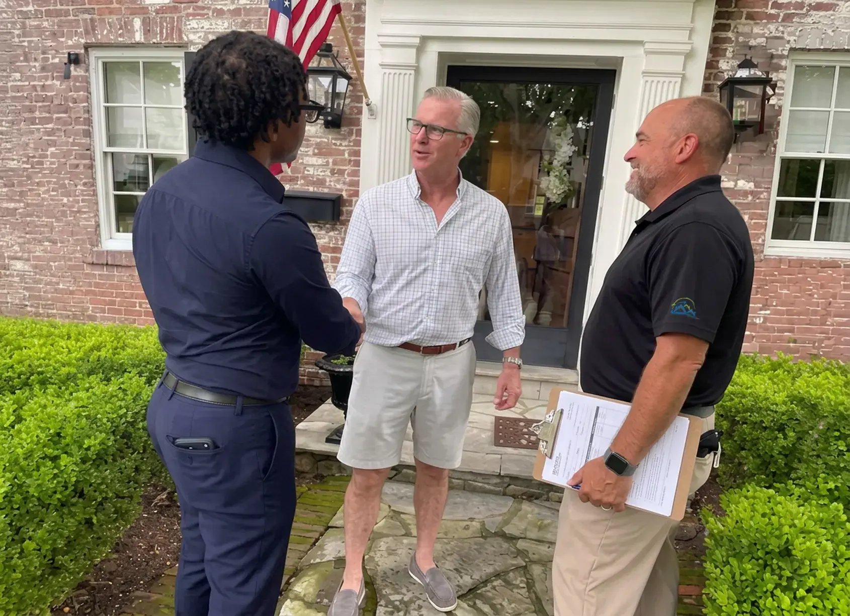 Two Hybrid Renovations team members shaking hands with a homeowner on the front walkway of a brick home