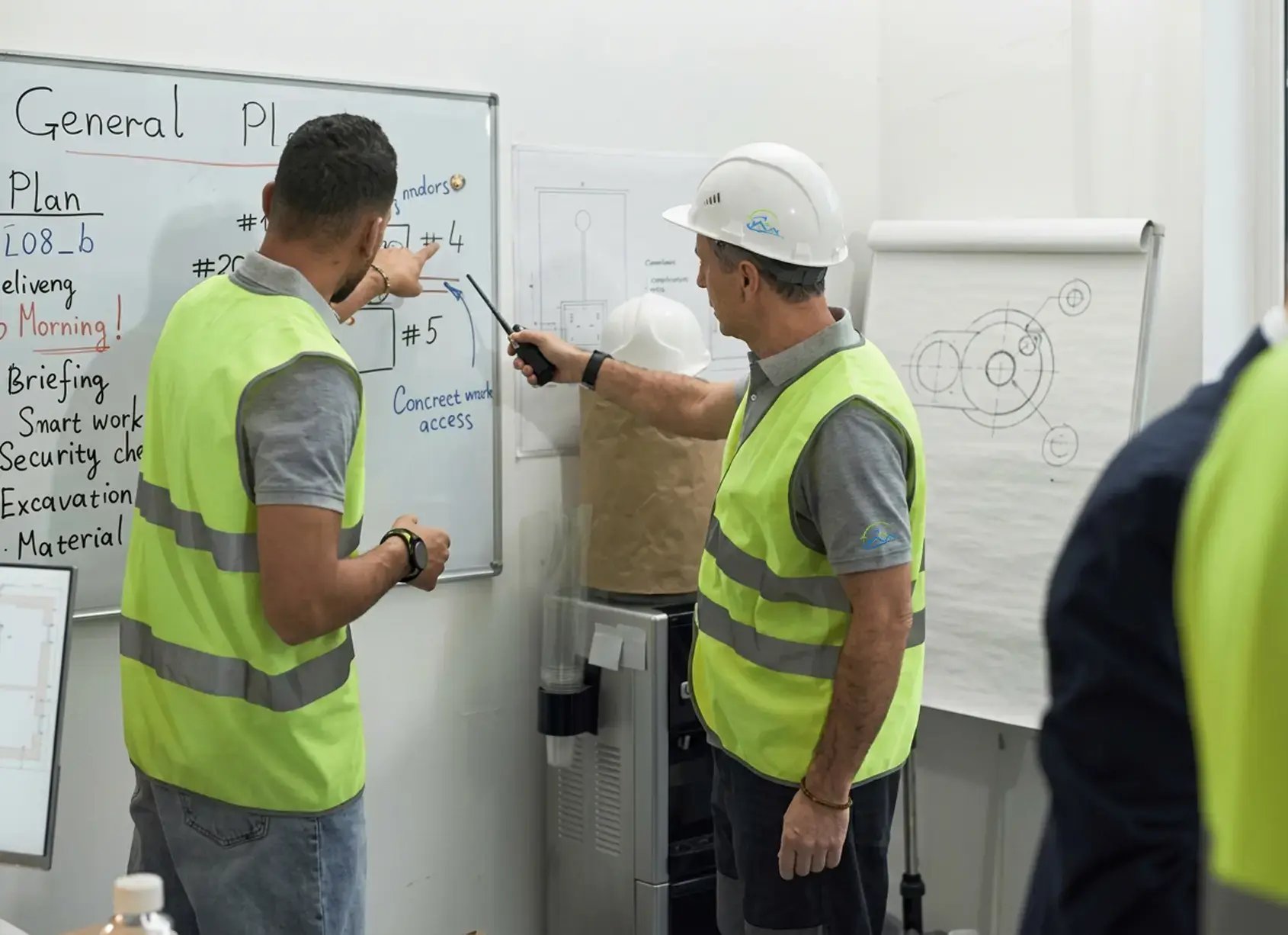 Two Hybrid Renovations team members in safety vests reviewing a project plan on a whiteboard during a briefing