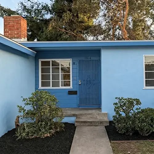 Bright blue stucco and lap siding with white-trimmed windows after exterior house painting — Hybrid Renovations