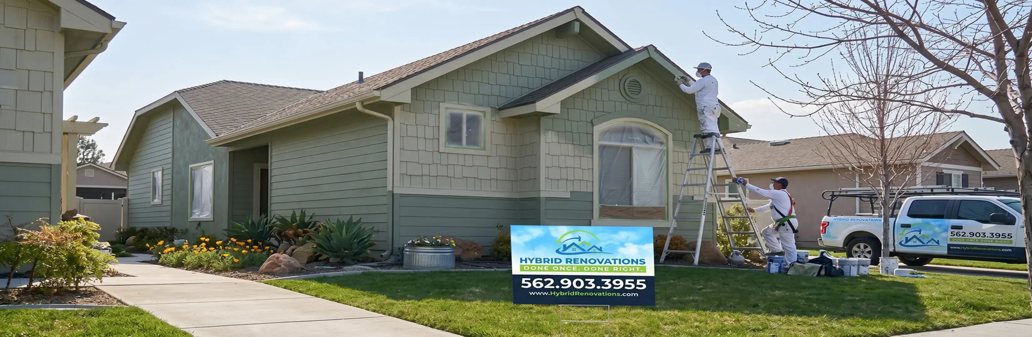Hybrid Renovations painters coating the trim and eaves of a green single-family home during exterior painting