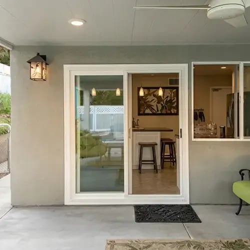 Covered back patio with stucco wall, white sliding glass door, and wood-beam ceiling after exterior renovation