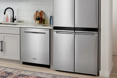 Stainless dishwasher and counter-depth refrigerator installed into white kitchen cabinetry
