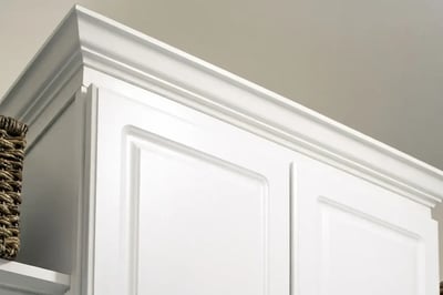 Crown molding and trim detail on the top of a white painted kitchen wall cabinet