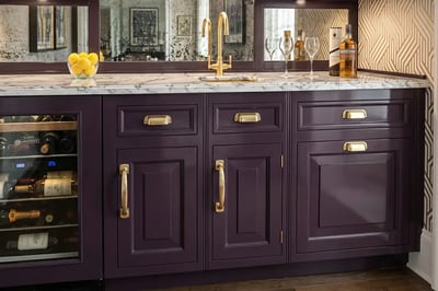 Deep aubergine raised-panel cabinets with brass cup pulls, marble top and a wine refrigerator