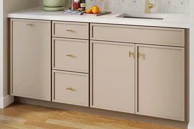 Greige shaker base cabinets and drawers with slim brass bar pulls under a white quartz counter