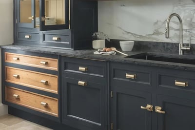 Navy inset cabinets with oak drawer fronts, brass cup pulls and a dark stone countertop
