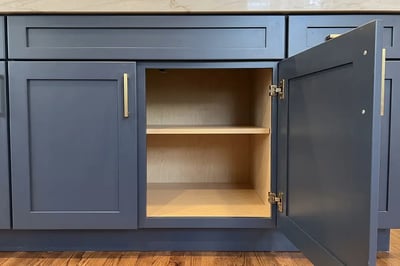 Open navy cabinet door revealing the plain plywood box behind a painted shaker front in a kitchen remodel