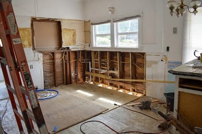 Kitchen mid-demolition with plaster removed, studs and wiring exposed and new subfloor going down