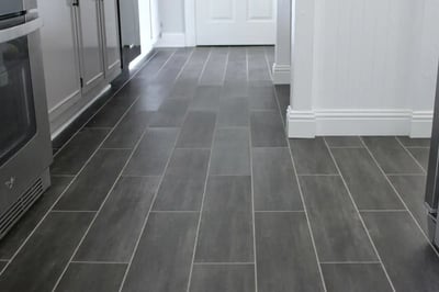 Grey wood-look porcelain plank tile flooring running between kitchen cabinets and a doorway