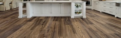 Wide plank wood-look luxury vinyl flooring running past a white kitchen island and cabinet run