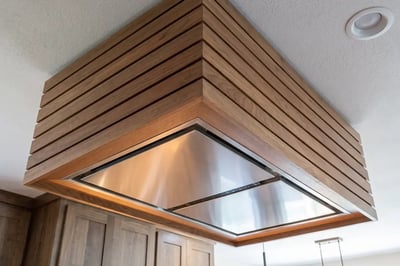 Slatted wood island hood with a stainless insert mounted to the ceiling above a kitchen island