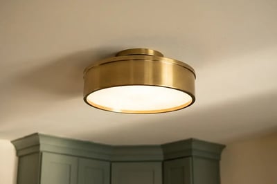 Lit brass flush mount ceiling light above sage green cabinets in a remodeled kitchen