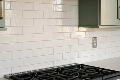 White subway tile backsplash in a running bond above a gas cooktop after a full kitchen replacement