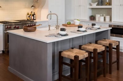 Grey kitchen island with a white quartz top, undermount sink and three woven bar stools