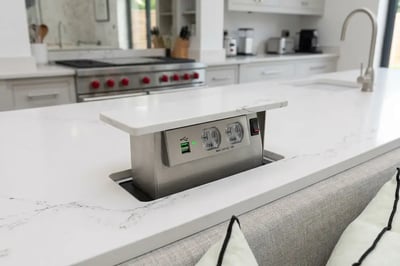 Pop-up countertop outlet with USB ports raised from a quartz kitchen island with bar seating