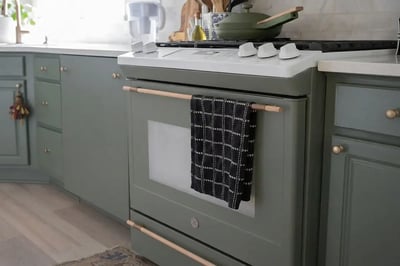 Freestanding kitchen range set between sage green cabinets with a towel on the oven handle