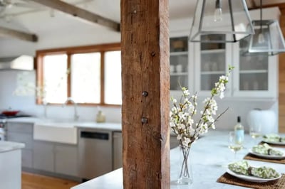 Reclaimed timber post beside a marble island in an open plan kitchen with exposed ceiling beams