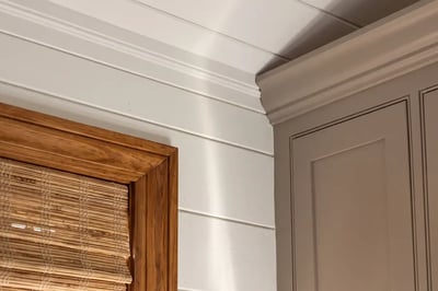 Painted cabinet crown meeting white shiplap and stained wood window trim in a kitchen remodel