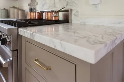 White marble countertop with a mitered edge and aged brass pull after a kitchen remodel