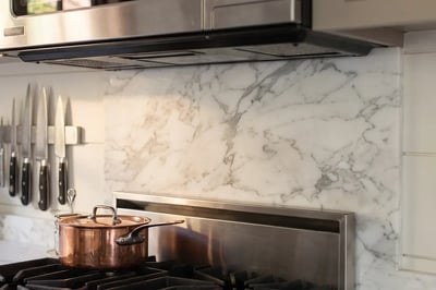 Full-height marble slab backsplash and knife strip above a stainless range after a kitchen remodel