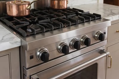 Stainless range cooktop with knurled control knobs and copper pots in a remodeled kitchen