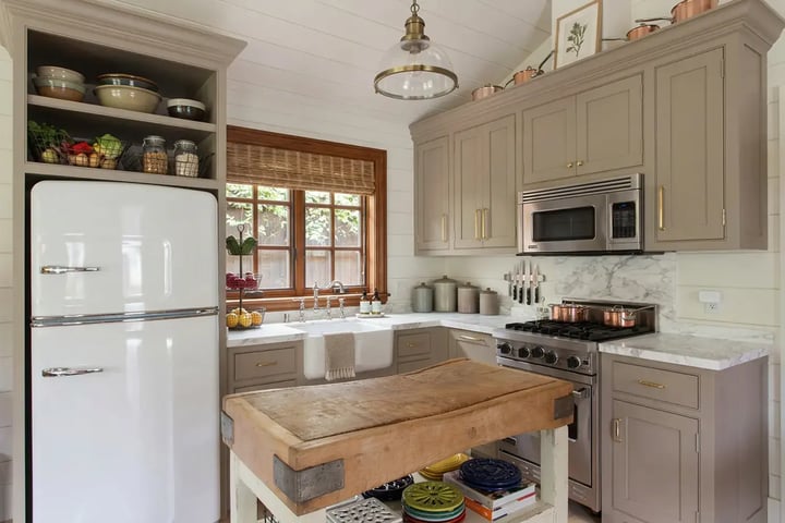 Refreshed kitchen with taupe cabinets, marble counters and a butcher block island under a glass pendant