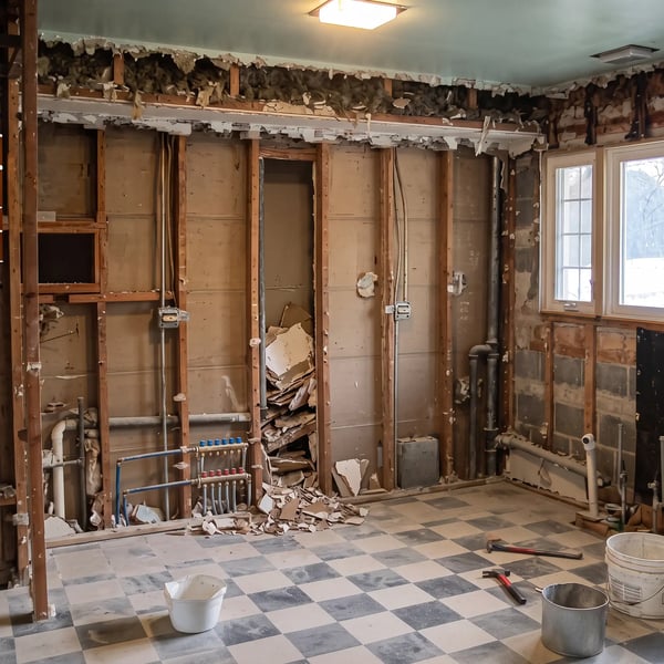 Kitchen stripped back to studs during demolition with exposed wiring, plumbing manifold and drain lines