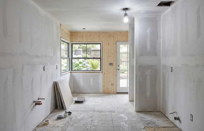 Galley kitchen mid-renovation at the drywall stage, with a new black-framed window, patio door, and pine paneling
