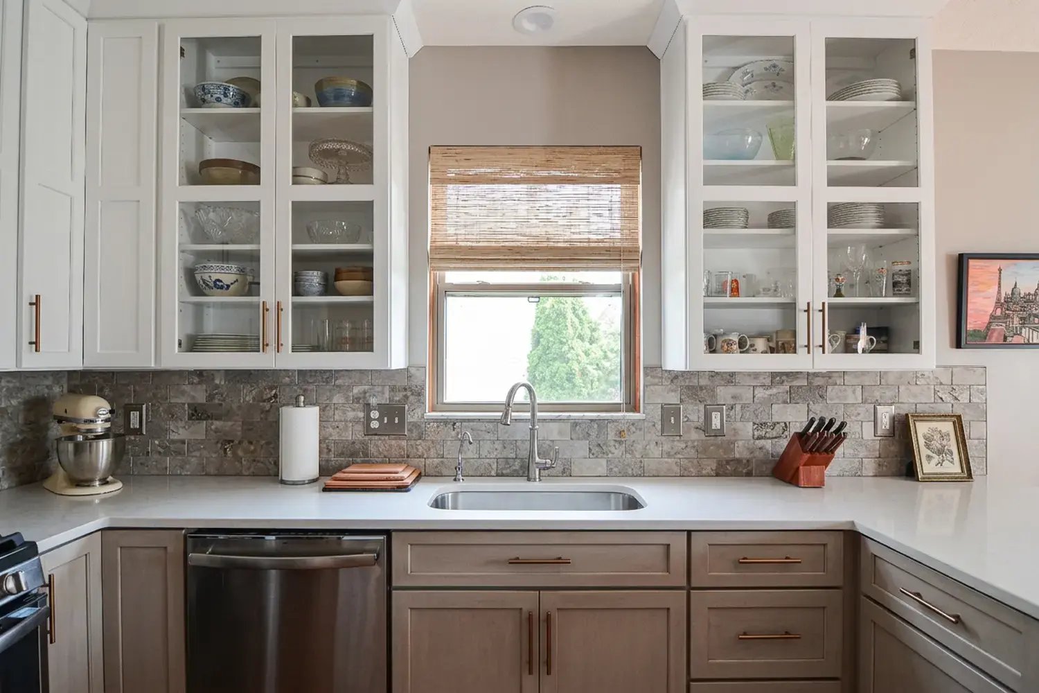 Two-tone kitchen cabinets with glass-front uppers and stone tile backsplash after a full kitchen remodel