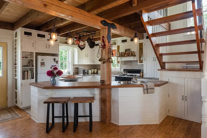 Open concept kitchen after wall removal with a peninsula, exposed beams and a support post at the opening