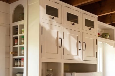 Off-white painted cabinets with glass front upper doors and bronze bail pulls in a farmhouse kitchen