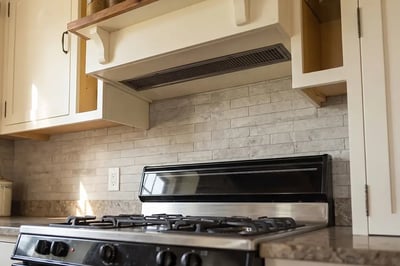 Recessed ventilation grille under a cabinet surround above a gas range with a tile backsplash