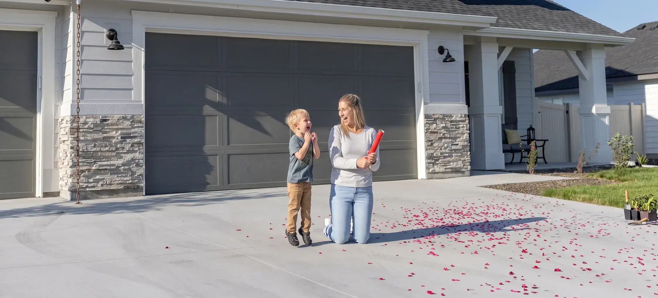 Smiling mother and young son celebrating on a new concrete driveway outside their renovated home