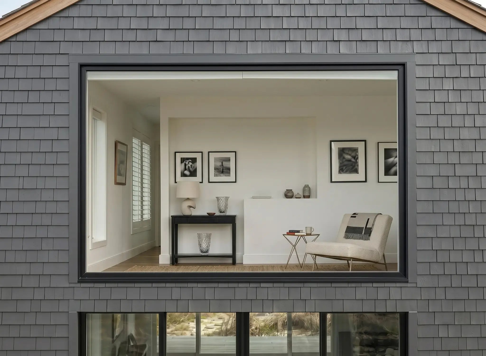 Large dark-framed picture window after installation on a gray shingle-sided home