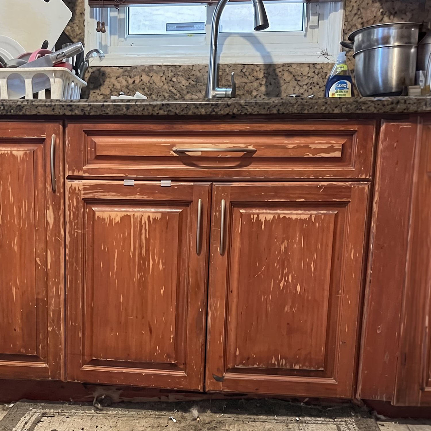 Kitchen cabinets with heavily worn and stripped finish above dated granite countertops before a remodel